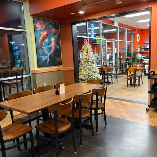 Restaurant dining area with wooden tables, chairs, koi fish artwork, glass entrance, and decorated Christmas tree.