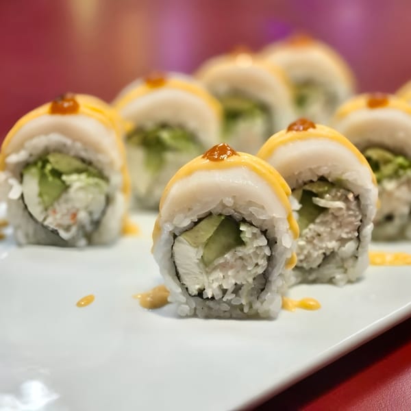 Close-up of Koto Teriyaki & Sushi's scallop and avocado sushi rolls with orange sauce on a white plate.