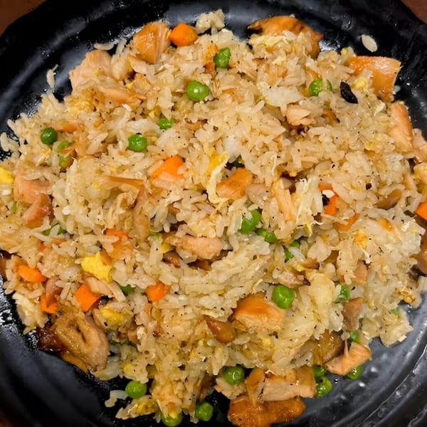 Salmon fried rice with peas, carrots, and scrambled egg on a black plate.