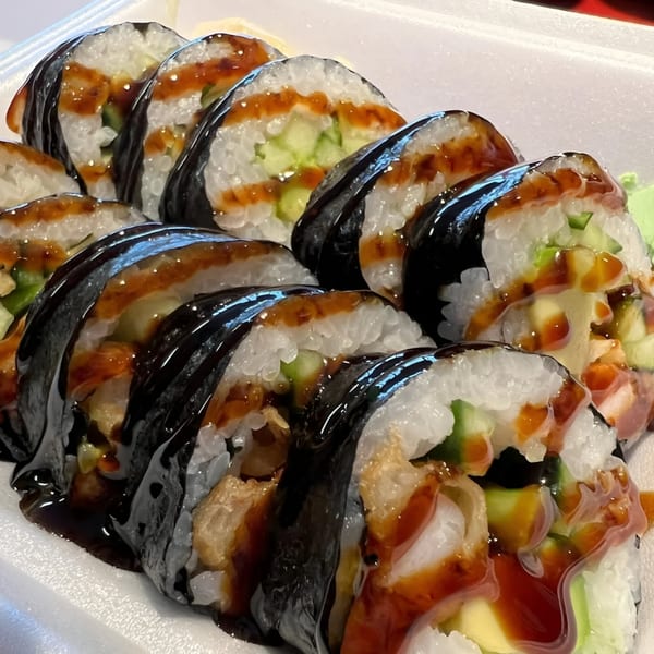 Close-up of Koto Teriyaki & Sushi's sushi rolls with dark sauce, cucumber, and tempura in a white container.